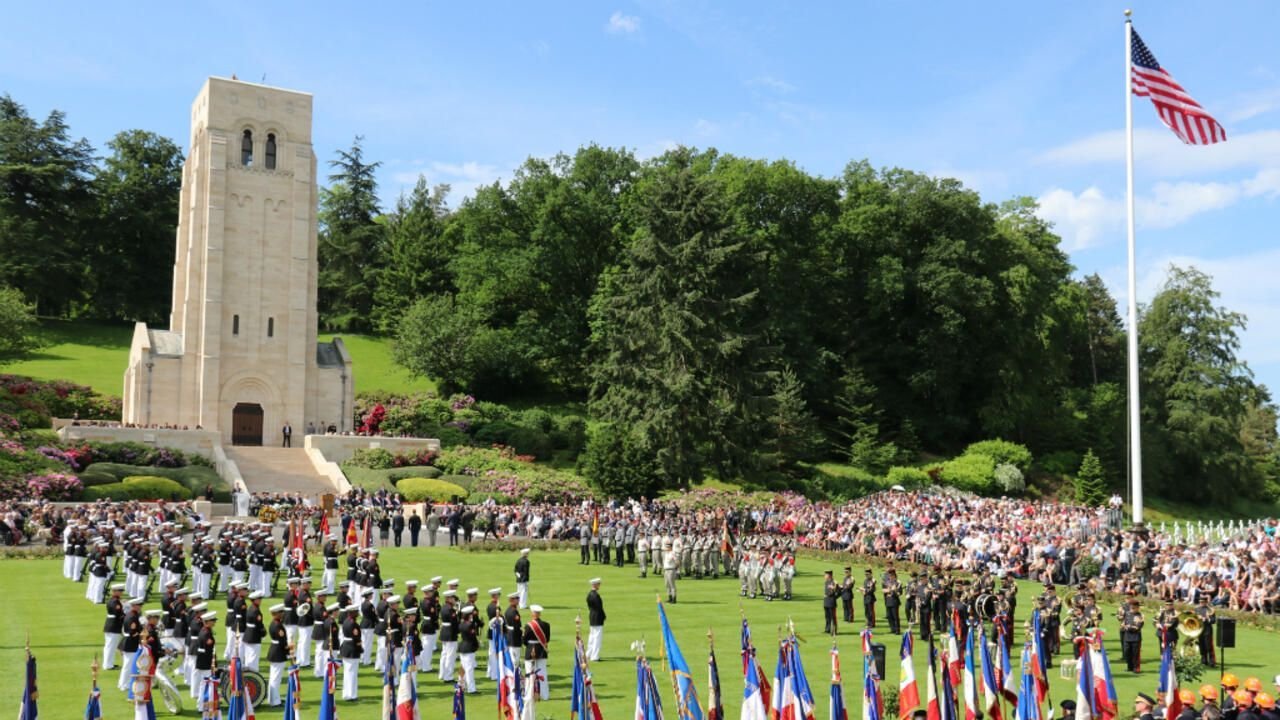 Un grand groupe de personnes se tient dans un champ avec des drapeaux devant une tour.